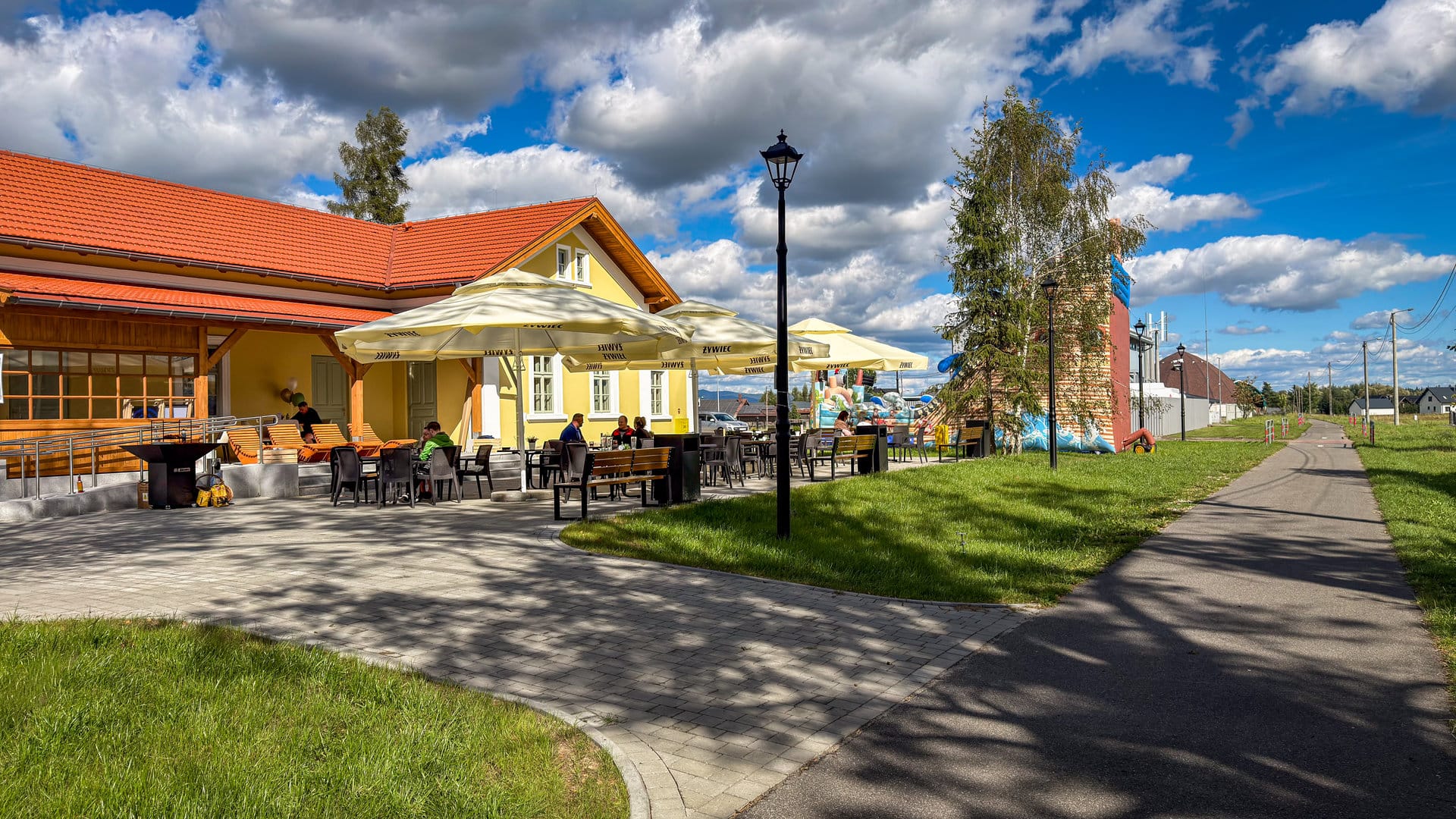 The Stacja Czarny Dunajec building with a terrace and parasols, next to a tarmac cycle path